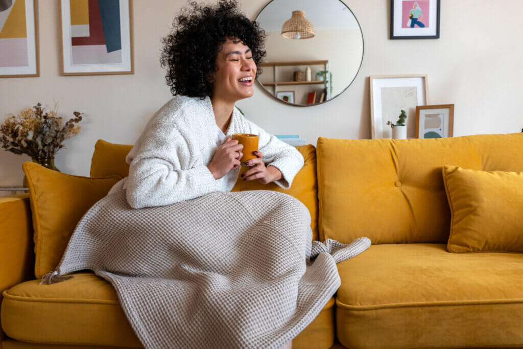 mulher negra no sofá com cobertor e xícara para representar como economizar energia no inverno