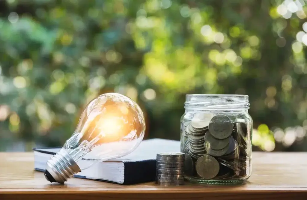 lâmpada e pote de moeda em cima da mesa para representar gestão de energia
