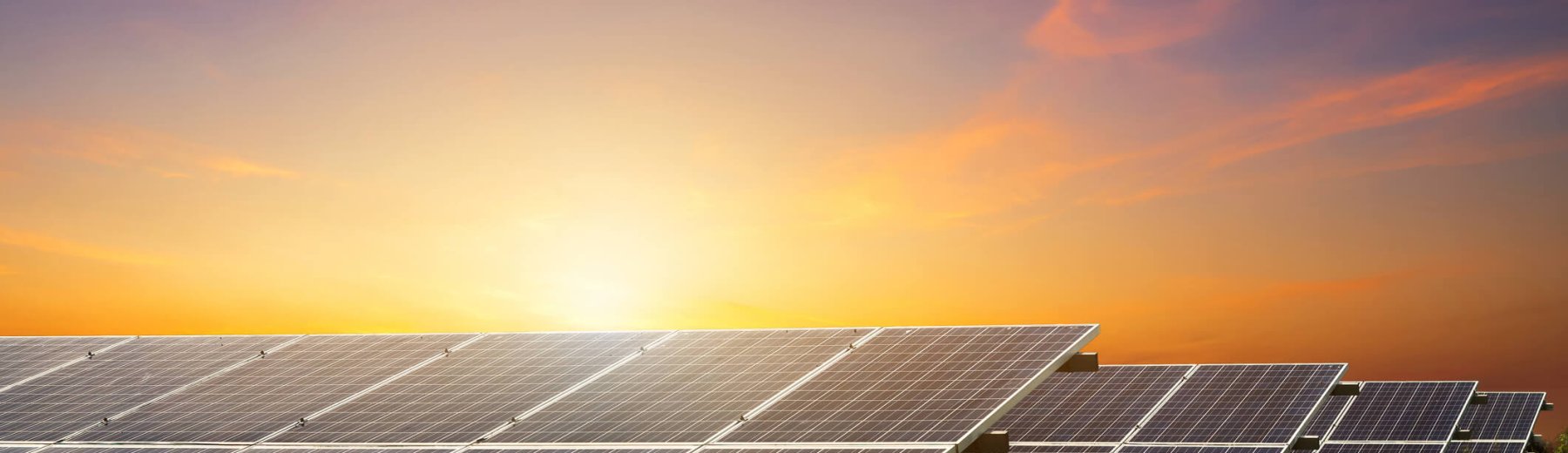 campo com painéis solares de um sistema fotovoltaico e pôr do sol atrás